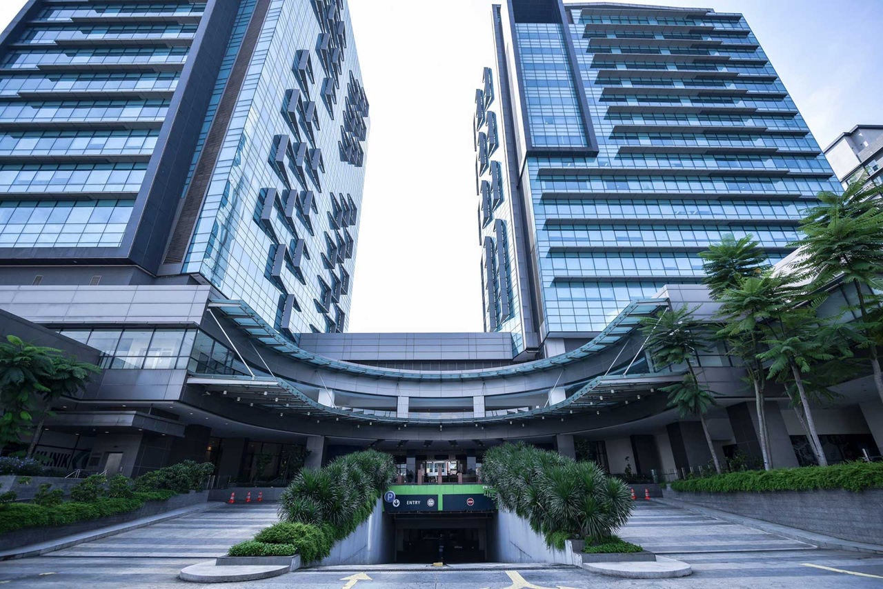 Exterior view of Puchong Financial Corporate Centre (PFCC) in Selangor, Malaysia, featuring two modern glass high-rise towers, landscaped entrance, and underground parking access.