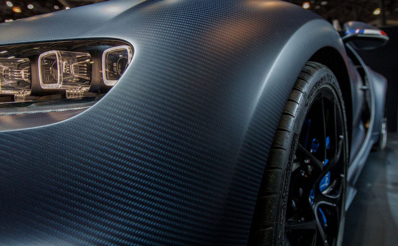 Close-up of carbon fiber body and LED headlight on front left side of luxury sports car with black alloy wheel